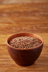 Top view close-up picture of flax seeds in a clay bowl on wooden background, selective focus, vertical.
