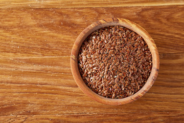 Top view on flax seeds in wooden bowl on rustic wooden background, selective focus.