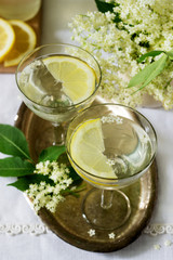 A cool drink with lemon and elderflower syrup in glasses on a metal tray. Rustic style.