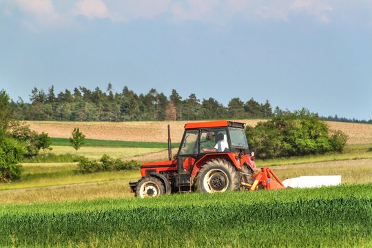 Old red tractor sails the meadow. Summer work on an agricultural farm.