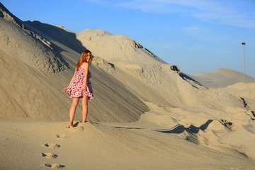 Piękna rudowłosa dziewczyna spaceruje po piaszczystych wydmach.