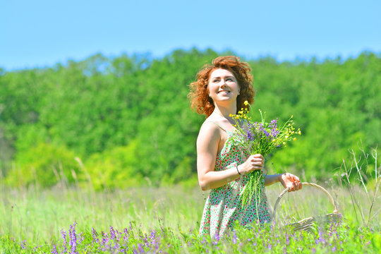 Summer landscape and beautiful smiling woman. A girl on a meadow in the forest with a bouquet of wildflowers and a wicker basket in her hands.