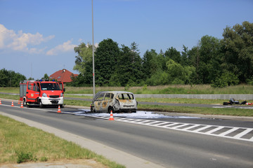 Spalony samochód osobowy na drodze, pożar ugaszony pianą przez straż pożarną.