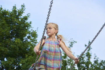  Little child blond girl having fun on a swing outdoor. Summer playground. Girl swinging high. Young child on swing outdoors
