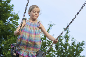  Little child blond girl having fun on a swing outdoor. Summer playground. Girl swinging high....