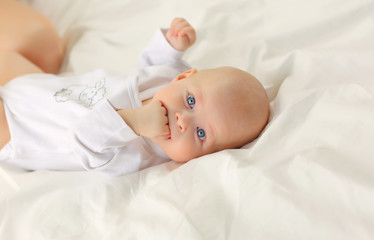 Baby lying in bed in white clothes.