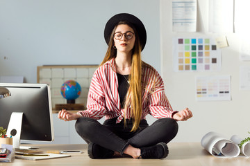 Pretty young business woman doing yoga on the table in the office.