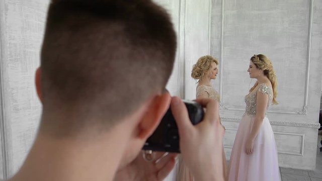 A photographer is photographing two girls on a white wall background.