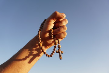 rosary in the hand of a man on the background of the sky - obrazy, fototapety, plakaty