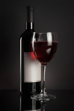 Red wine bottle and full wineglass on black