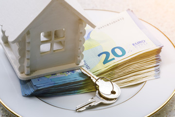 House model, a bundle of money and keys are on a white plate