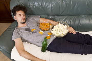 Tired young man sleeping on a sofa with food after party