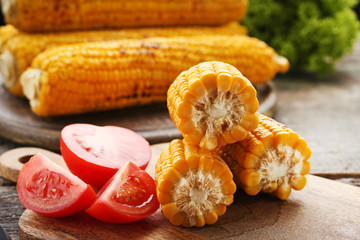 Tasty grilled corns with tomatoes on grey wooden table