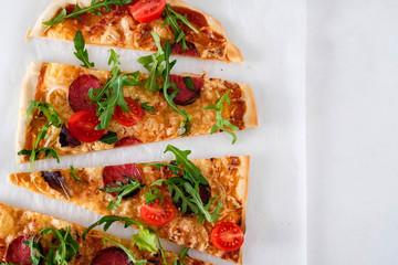 Flatbread pizza garnished with fresh arugula on wooden pizza board, top view. Dark stone background