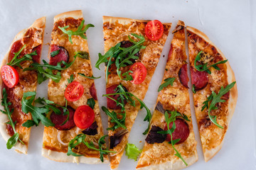 Flatbread pizza garnished with fresh arugula on wooden pizza board, top view. Dark stone background