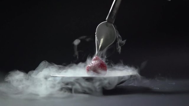 The liquid flows from the curved spoon to the berry.