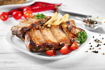 Plate with delicious grilled ribs and vegetable garnish on table