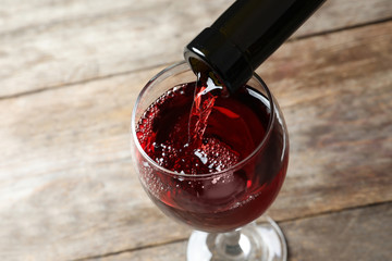 Pouring delicious red wine into glass on wooden background