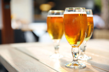Glasses with cold beer on table against blurred background
