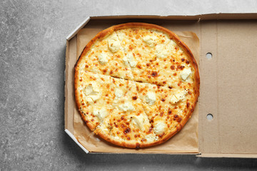 Carton box with delicious pizza on grey background, top view