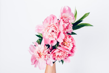 Woman's hand holds bouquet of light pink peonies