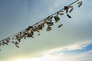 a lot of pairs of shoes hung on a rope for tied shoelaces, against a cloudy sky