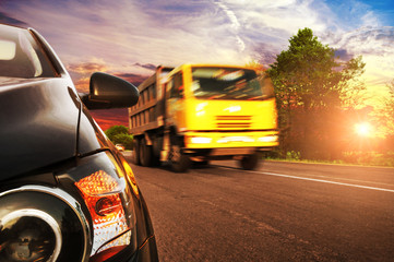 Obraz na płótnie Canvas Close-up of a car on a countryside road with a truck driving fast against sky with sunset