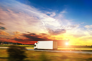 Box truck driving fast on the countryside road against night sky with sunset