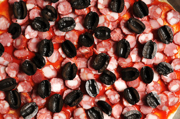 Close-up of sliced olives, sausages with sauce on a pizza dough
