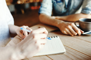 Hands of woman making notes in her notepad while discussing business ideas with her male partner...