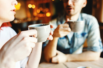 Young couple drinking coffee in cafe and chatting, focus on woman holding cup in her hands