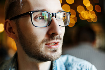 Face of intelligent young man with stubble beard wearing eyeglasses and looking away thoughtfully,...