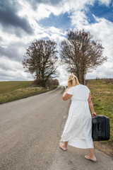 Frau in wei&szlig;em Kleid marschiert mit Koffer entlang Stra&szlig;e