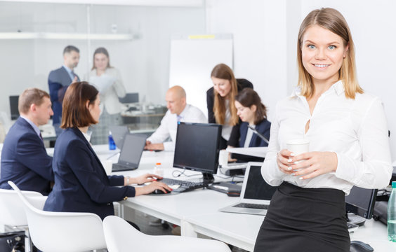 Positive young business woman foreground in busy open plan office