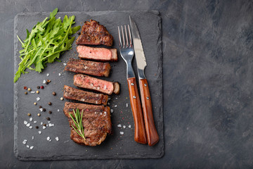 Closeup ready to eat steak new York beef breeds of black Angus with herbs, garlic and butter on a stone Board. The finished dish for dinner on a dark stone background. Top view with copy space