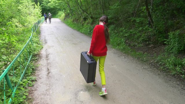 girl, walks through the woods with a heavy black suitcase. 4k, slow-motion shooting, steadicam shot.