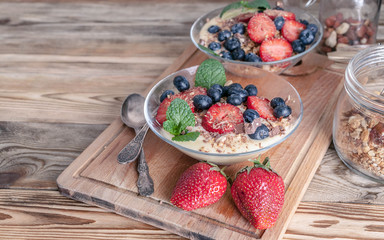 Granola with nuts, yogurt, fresh blueberries and strawberries in a glass bowl on a wooden background