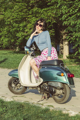 Fototapeta na wymiar Beautiful young woman sits on scooter. Stylish girl on a moped.
