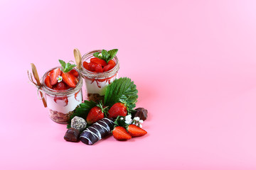 two glasses of healthy fresh strawberry yogurt with fresh berries, oatmeal cookies wooden spoon, chocolate and mint Isolated on pink background, healthy breakfast. copy space, set