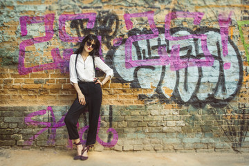 Stylish young woman on graffiti background. Portrait of a fashionable female in sunglasses.