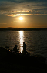Naklejka na ściany i meble Fishermen on the background of the lake and the evening sun