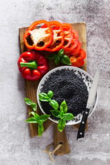 red, ripe, bell pepper cut on a cutting board and fresh basil leaves. Black lentils and knife . Background of cooking food on grey stone