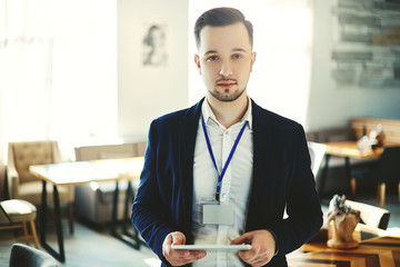 Confident young delegate with stubble beard posing with tablet computer at business event, blank id...