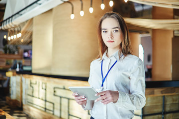 Portrait of young female manager looking at camera with tablet computer in her hands and badge...