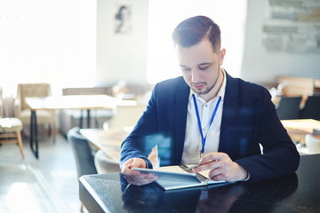 Young businessman with id card around his neck pointing with pen at tablet computer screen while...