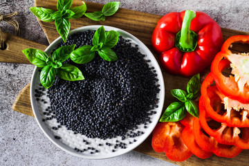 red, ripe, bell pepper cut on a cutting board and fresh basil leaves. Black lentils. Background of cooking food on grey stone