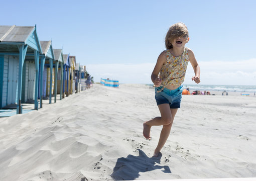 Girl running with hair over face on the beach and beach huts