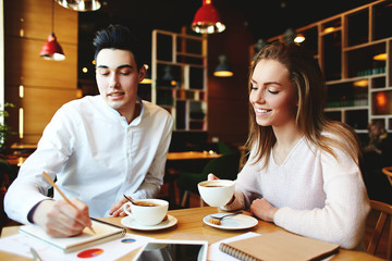 Young businessman and businesswoman drinking coffee and sharing ideas sitting at table in cozy cafe.