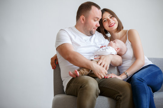 Photo of happy married couple with newborn baby sitting on sofa