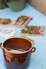 Homemade lard in clay pots, sausage and brined pickles set up on a table at a rustic garden party